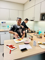 Eine der Pflegekräfte schneidet Chilli auf einem Brett, während eine andere Person im Hintergrund in einem Topf rührt