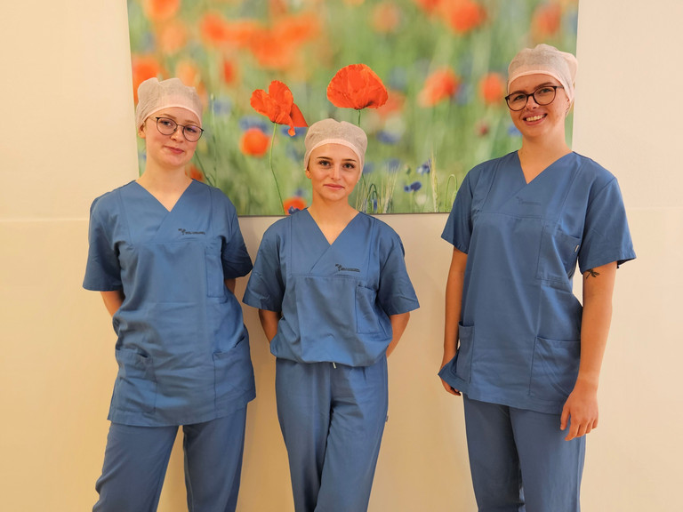 Auszubildende zur OTA und ATA im Immanuel Klinikum Bernau stehen nebeneinander vor einer Wand mit einem Bild Auszubildende zur OTA und ATA im Immanuel Klinikum Bernau stehen nebeneinander vor einer Wand mit einem Bild