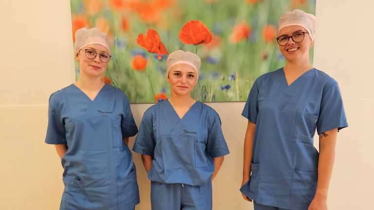 Auszubildende zur OTA und ATA im Immanuel Klinikum Bernau stehen nebeneinander vor einer Wand mit einem Bild