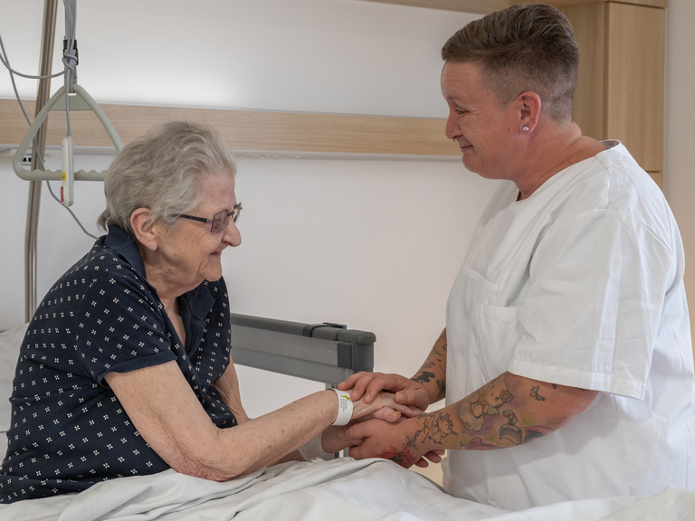 Pflegeassistenz hält Hand von Patientin - Immanuel Klinikum Bernau