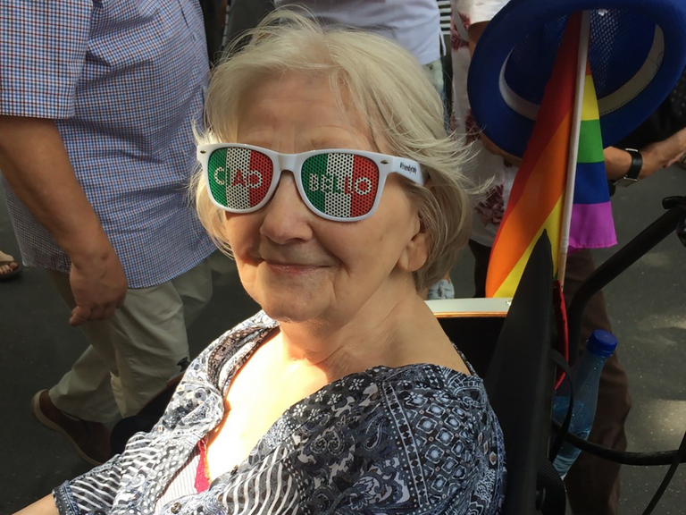 Seniorin im Rollstuhl auf schwul-lesbischem Stadtteilfest Berlin mit einer Regenbogenfahne
