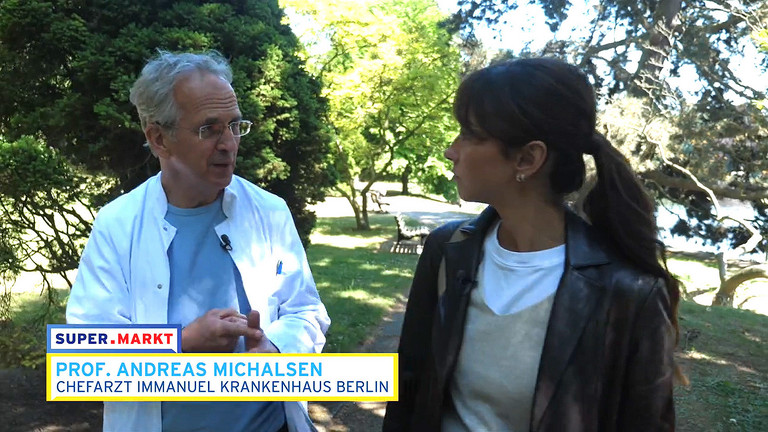 Screenshot Pro. Michalsen im Gespräch mit Frau im Park und einer Bauchbinde der Sendung Screenshot Pro. Michalsen im Gespräch mit Frau im Park und einer Bauchbinde der Sendung
