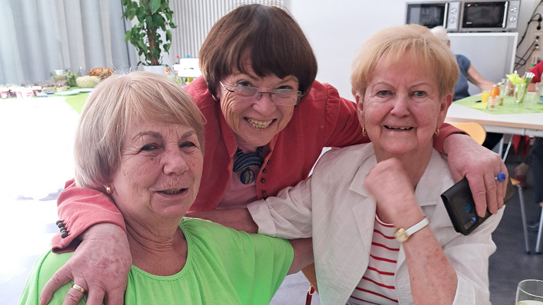 Drei ehemalige Kolleginnen beim Ehemaligentreffen des Immanuel Klinikum Bernau Arm in Arm an einem Tisch