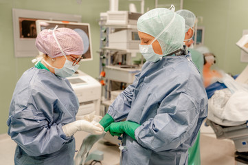 Eine Person in OP Kleidung hilft einer anderen Person in OP Kleidung beim Anlegen eines Handschuhs in einem OP Saal im Albertinen Krankenhaus Hamburg Schnelsen