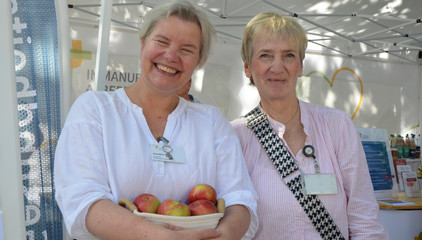 Zwei Mitarbeiterinnen blicken fröhlich in die Kamera an den Ständen des Gesundheitscampus Volksdorf der Immanuel Albertinen Diakonie beim Stadtteilfest Volksdorf in Hamburg