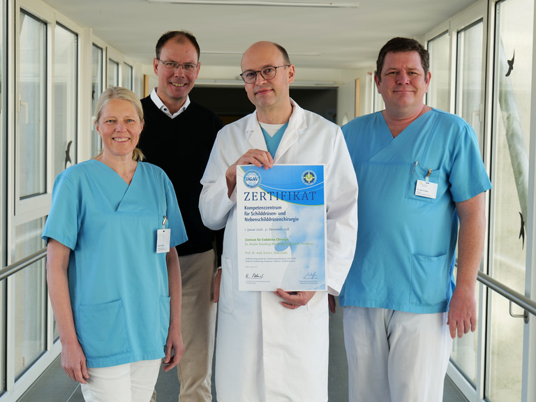 Vier Mitarbeitende des Evangelischen Amalie Sieveking Krankenhauses stehen nebeneinander und präsentieren die DGAV-Zertifizierung für das Zentrum für Endokrine Chirurgie: Dr. Denise Wittek, Geschäftsführer Andreas Schneider, Prof. Dr. Ernst von Dobschütz und Oberarzt Alexander Gnoss.