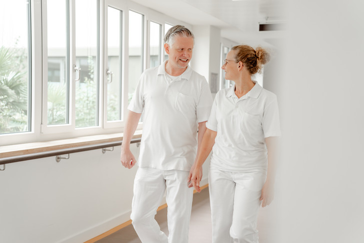 Ein Therapeut und eine Therapeutin in weißer Funktionskleidung gehen über einen Stationsflur und unterhalten sich im Zentrum für Altersmedizin im Albertinen Krankenhaus in Hamburg-Schnelsen Ein Therapeut und eine Therapeutin in weißer Funktionskleidung gehen über einen Stationsflur und unterhalten sich im Zentrum für Altersmedizin im Albertinen Krankenhaus in Hamburg-Schnelsen