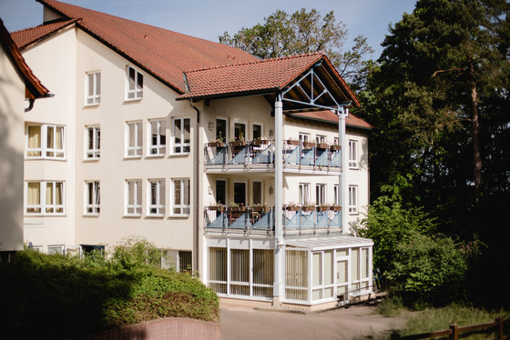 Blick auf das Gebäude mit Bäumen und Pflanzen im Vordergrund und Balkonen mit Blumen der Senioreneinrichtung Immanuel Haus Ecktannen in Waren (Müritz)