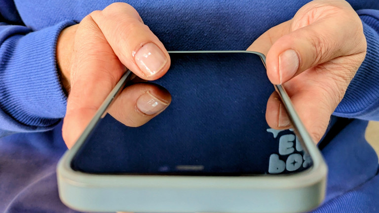 Person hält Smartphone in den Händen und hält beide Daumen auf Bildschirm
