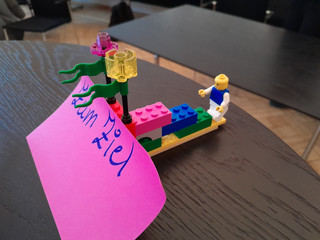 Ein Segelboot aus bunten Legosteinen mit einem lila Papierstück mit der Aufschrift "Zum Ziel" auf dem Tisch beim Teamtag vom Meisterbetrieb für Handwerk Werkstück Berlin zum Thema "Gute Kommunikation verbindet" in Berlin-Wannsee Ein Segelboot aus bunten Legosteinen mit einem lila Papierstück mit der Aufschrift "Zum Ziel" auf dem Tisch beim Teamtag vom Meisterbetrieb für Handwerk Werkstück Berlin zum Thema "Gute Kommunikation verbindet" in Berlin-Wannsee