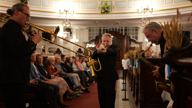 Ein Blechbläser läuft musizierend und in Begleitung von zwei anderen Bläsern des Trios "Windspiel" der NDR Bigband durch die mit Publikum besetzten Kirchengänge beim 10. Herzbrücke-Benefizkonzert im Hamburger „Michel“ der Albertinen-Stiftung. Ein Blechbläser läuft musizierend und in Begleitung von zwei anderen Bläsern des Trios "Windspiel" der NDR Bigband durch die mit Publikum besetzten Kirchengänge beim 10. Herzbrücke-Benefizkonzert im Hamburger „Michel“ der Albertinen-Stiftung.