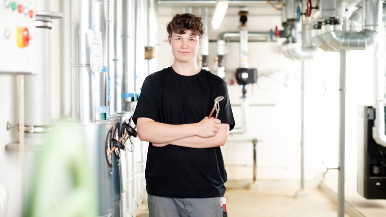 Auszubildender mit einer Zange in der Hand blickt in Kamera