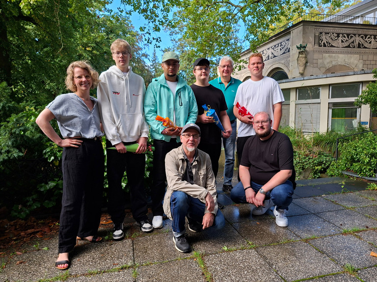 Gruppenbild der neuen Auszubildenden bei Werkstück mit Geschäftsführer und Mitarbeitenden auf der Terrasse der Wannse-Villa